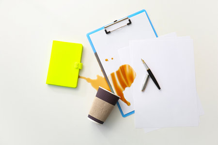 Stationery, overturned cup and spilled coffee on office tableの写真素材