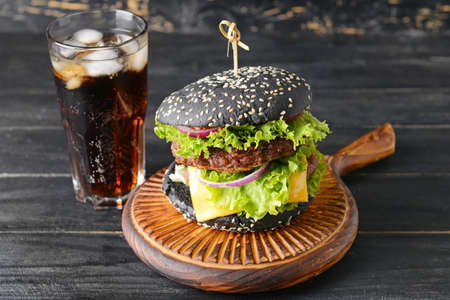 Tasty burger with black bun and cola drink on tableの写真素材