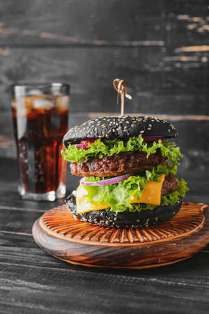 Tasty burger with black bun and cola drink on tableの写真素材