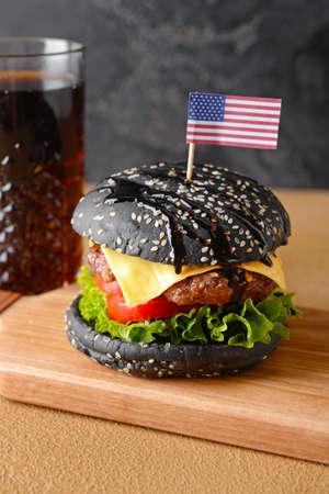 Tasty burger with black bun and cola drink on tableの写真素材