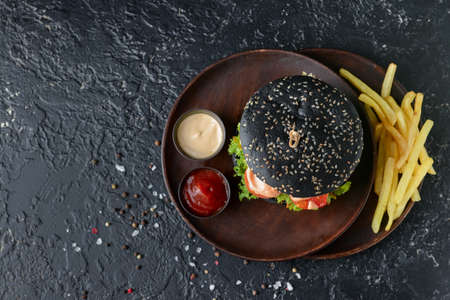 Tasty burger with black bun and french fries on dark backgroundの写真素材