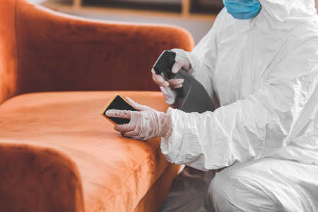 Worker in biohazard costume removing dirt from sofa in houseの写真素材