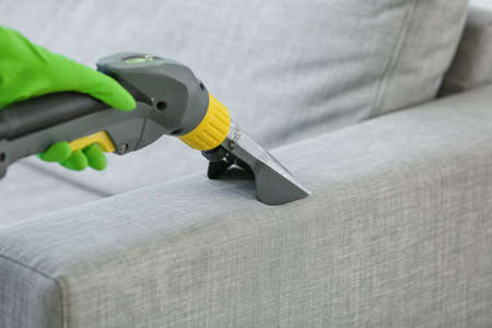 Dry cleaner's employee removing dirt from sofa in houseの写真素材