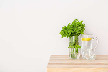 Glass with fresh mint and jug of lemon water on table in kitchenの写真素材