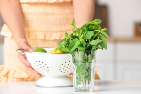 Glass with fresh mint on table and blurred woman with citruses in kitchenの写真素材