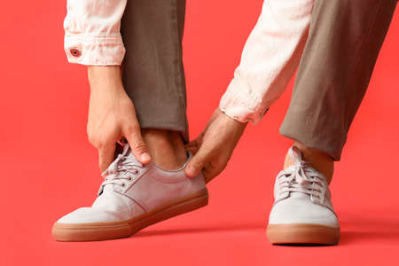 Young man putting on stylish shoes on color backgroundの写真素材