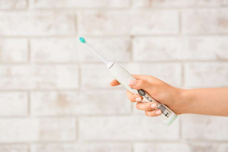 Female hand with electric tooth brush on brick backgroundの写真素材