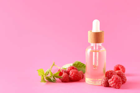 Bottle of raspberry essential oil on color background