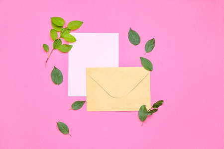 Envelope with paper sheet and green leaves on color background