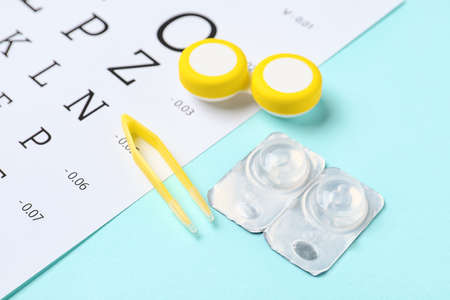 Container with contact lenses, tweezers and eye test chart on color backgroundの写真素材