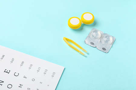 Container with contact lenses, tweezers and eye test chart on color backgroundの写真素材