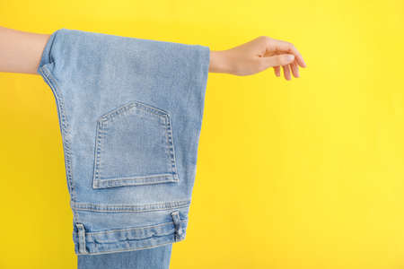 Female hand with stylish jeans pants on color backgroundの写真素材