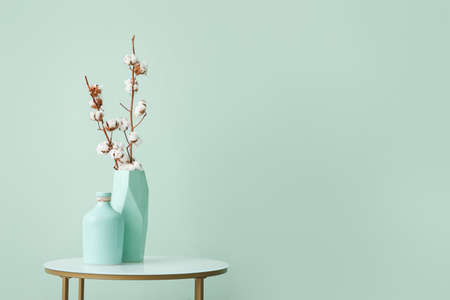 Vases with cotton flowers on stylish table near color wall in roomの写真素材