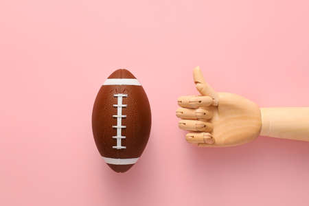 Hand of mannequin with rugby ball on color background