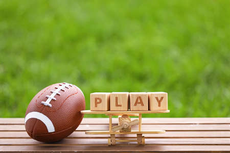 Rugby ball with wooden airplane and cubes with word PLAY on table outdoorsの写真素材