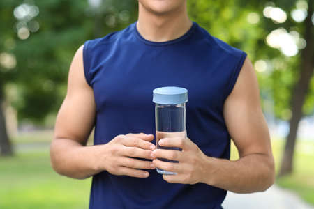 Sporty young man with bottle of water in park, closeupの写真素材