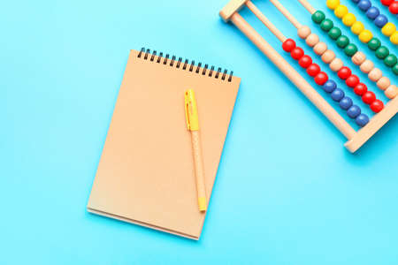 Wooden abacus with notebook and pen on color background