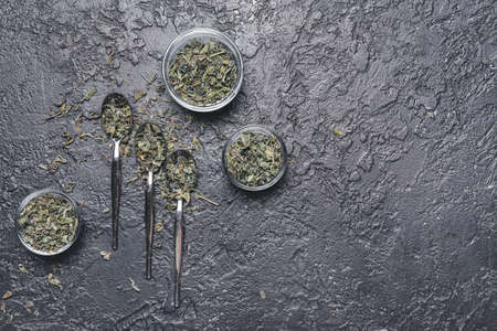 Spoons and bowls with dry green tea on dark backgroundの写真素材