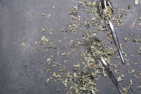 Spoons with dry green tea on dark background
