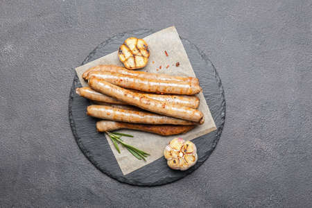 Slate plate with delicious grilled sausages and garlic on dark background