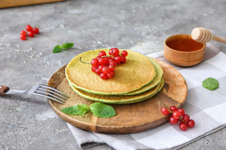 Plate with tasty green pancakes and berries on gray background