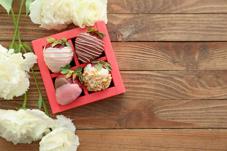 Box with tasty glazed strawberry and flowers on wooden backgroundの写真素材