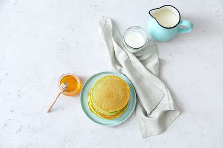 Plate with tasty green pancakes, milk and honey on white background