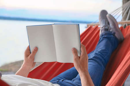 Young man reading book while relaxing in hammock outdoorsの写真素材