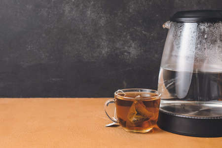 Modern electric kettle and cup of tea on tableの写真素材