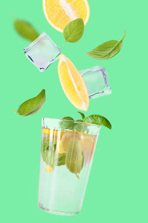 Glass of tasty lemonade with flying ingredients on color backgroundの写真素材