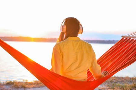 Young woman listening to music while relaxing in hammock outdoorsの写真素材