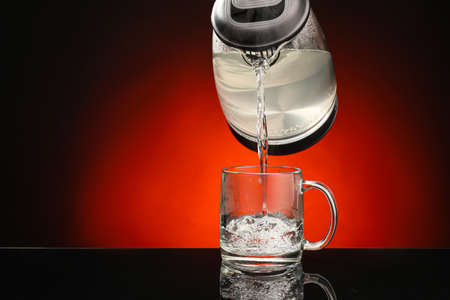 Pouring of hot water from kettle in mug on color backgroundの写真素材