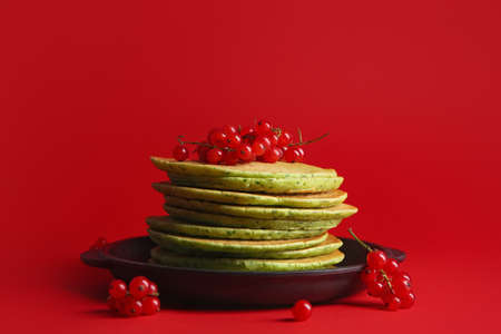 Frying pan with tasty green pancakes and berries on color backgroundの写真素材