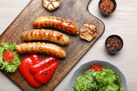 Wooden board with delicious grilled sausages, vegetables and spices on tableの写真素材