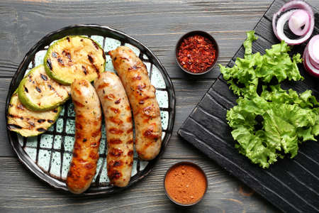 Plate with delicious grilled sausages, vegetables and spices on tableの写真素材
