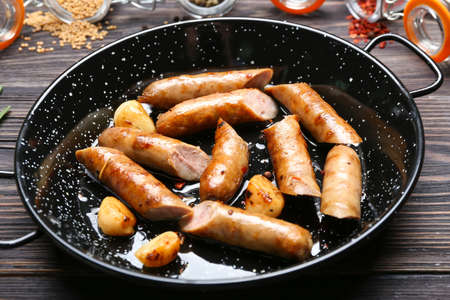 Frying pan with delicious grilled sausages on wooden tableの写真素材