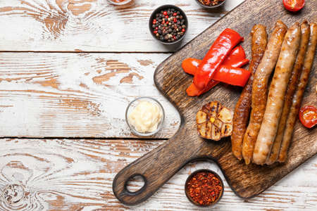 Wooden board with delicious grilled sausages, vegetables and spices on wooden tableの写真素材