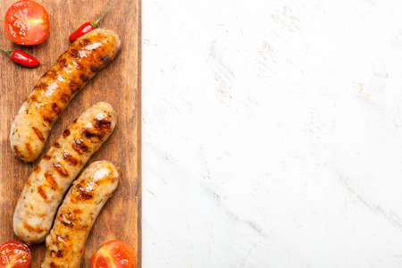 Wooden board with delicious grilled sausages and vegetables on light backgroundの写真素材
