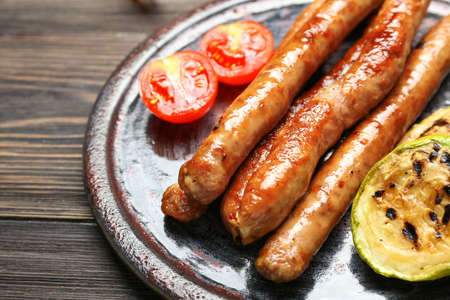 Plate with delicious grilled sausages and vegetables on wooden table, closeupの写真素材