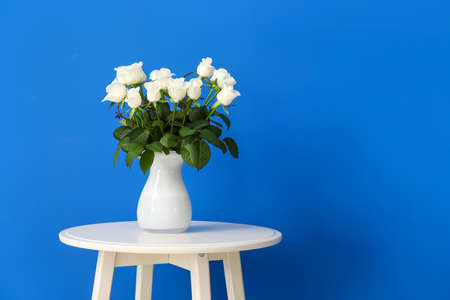Beautiful vase with roses on table near color wall