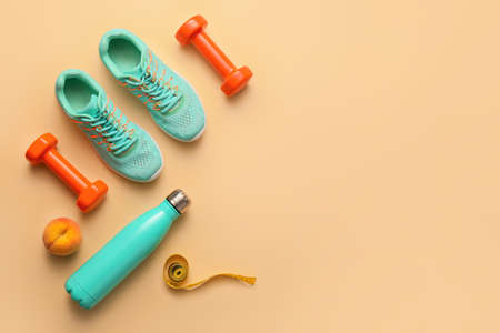 Dumbbells with shoes, bottle for water and measuring tape on color backgroundの写真素材