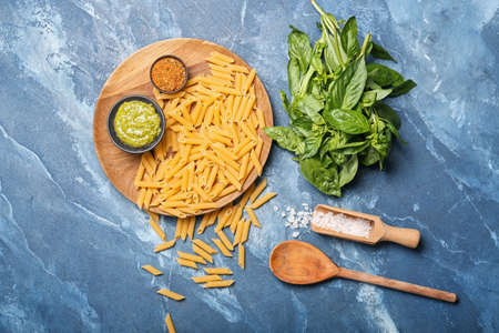 Wooden plate with raw pasta and ingredients on color backgroundの写真素材