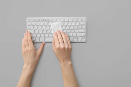 Woman cleaning computer keyboard on light background