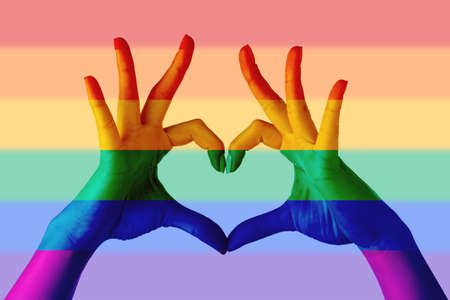 Woman making heart with her hands painted in colors of LGBT flag on rainbow backgroundの写真素材