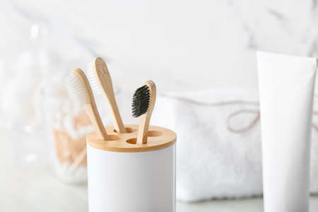 Holder with wooden toothbrushes and toothpaste on table in bathroom