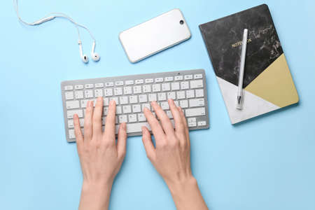 Female hands with computer keyboard, gadgets and stationery on color background