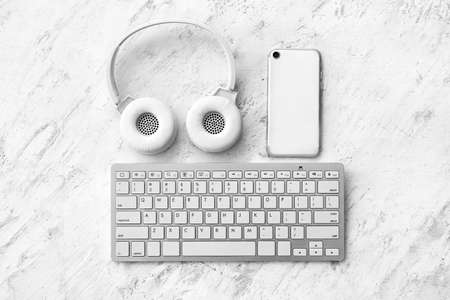 Computer keyboard, headphones and mobile phone on light background