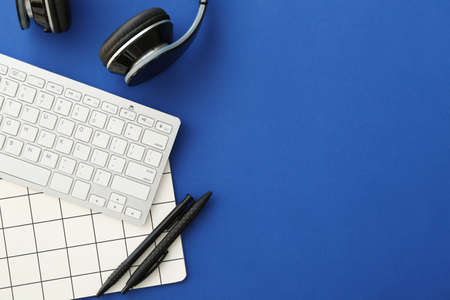 Computer keyboard, headphones and stationery on color background