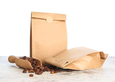 Bags with coffee beans and scoop on table against white backgroundの写真素材