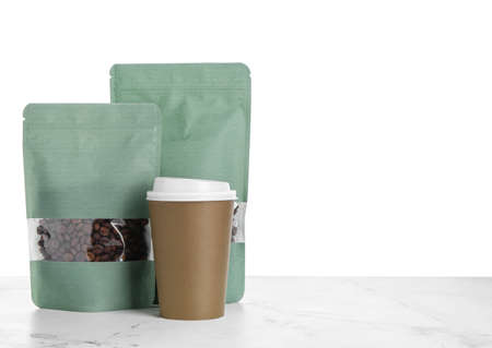 Bags with coffee beans and cup on table against white background